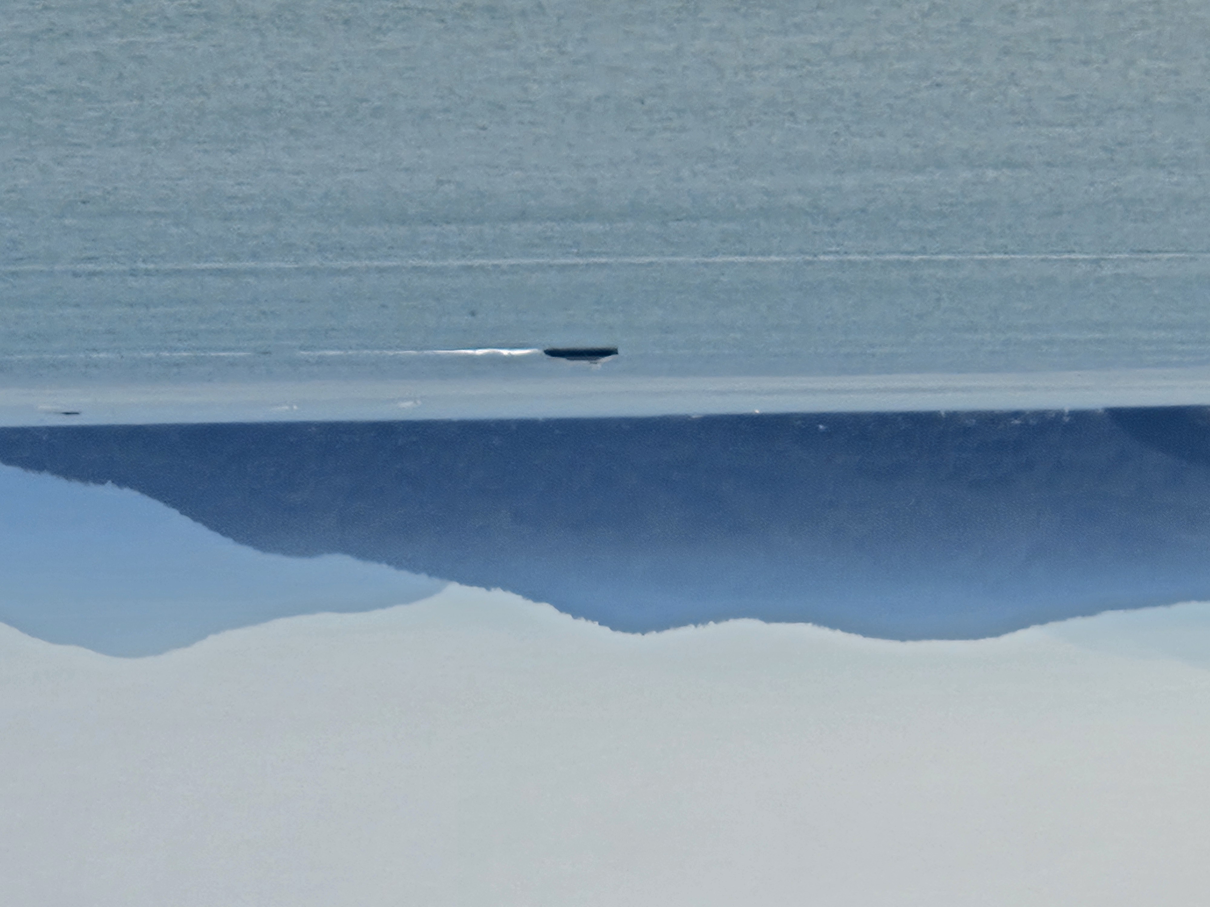 A small vessel crossing Pacific coastal waters beneath layered mountain ranges